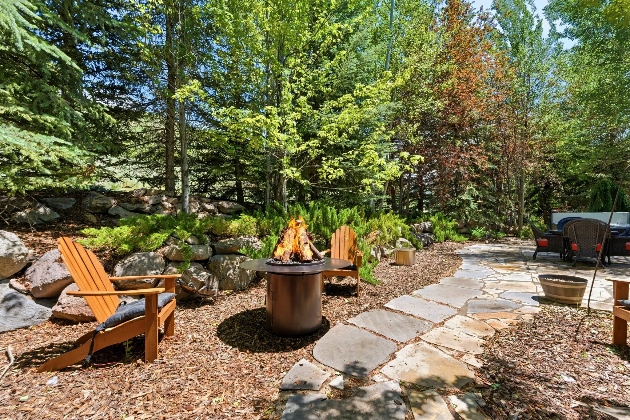 Outdoor fire pit area featuring a stone retaining wall and surrounding mature trees