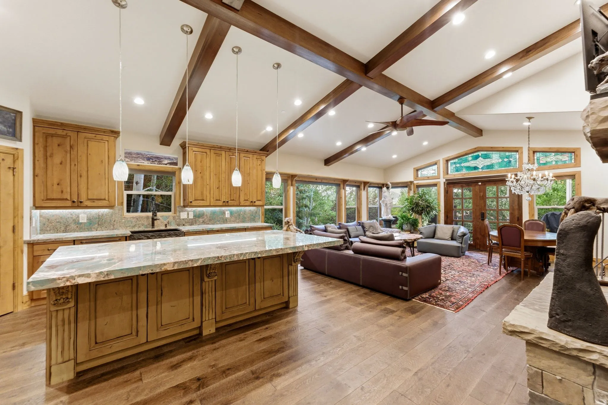Open-concept living area featuring a vaulted ceiling with exposed wood beams, hardwood flooring, and a stone fireplace