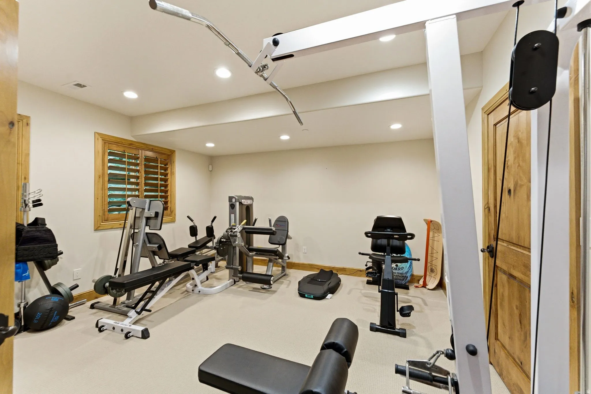 Dedicated fitness space with recessed lighting, light-colored walls, and a window featuring natural wood plantation shutters