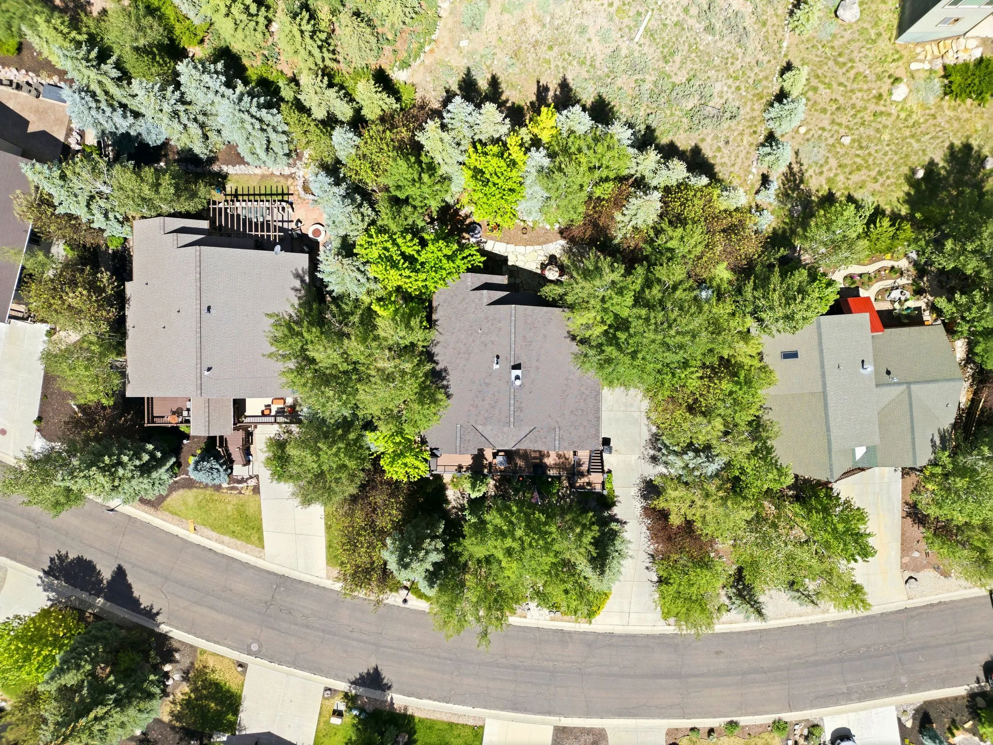 Aerial perspective highlighting a residential property with a dark shingle roof, a concrete driveway, and surrounding mature trees