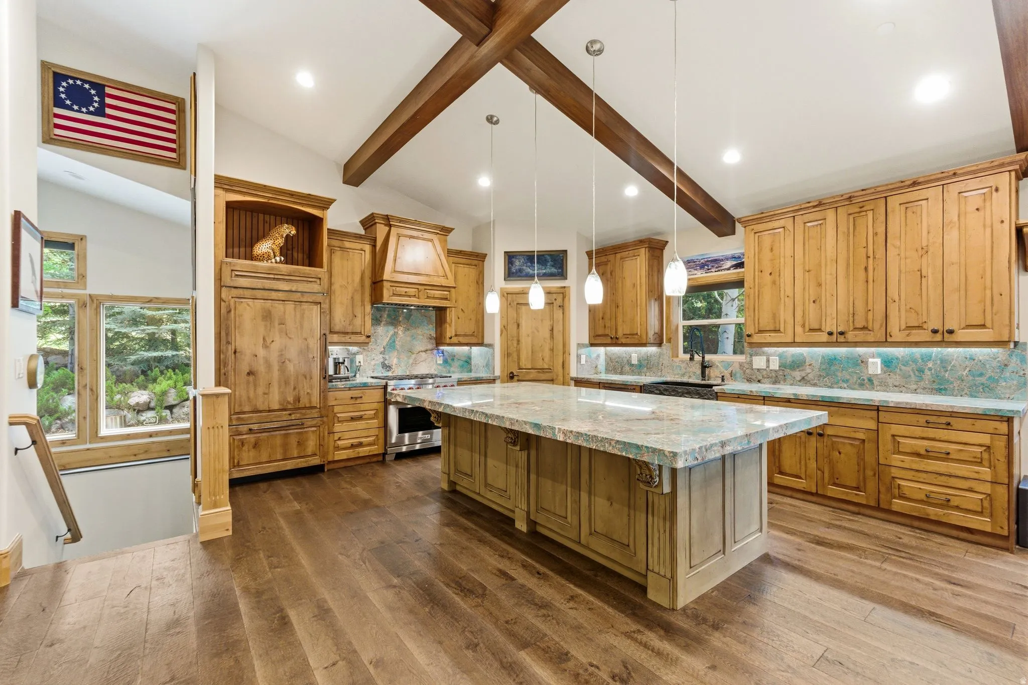 Spacious kitchen featuring vaulted ceilings with exposed wood beams, wood-finish flooring, custom wood cabinetry, a large center island with a light-toned countertop, and a tiled backsplash