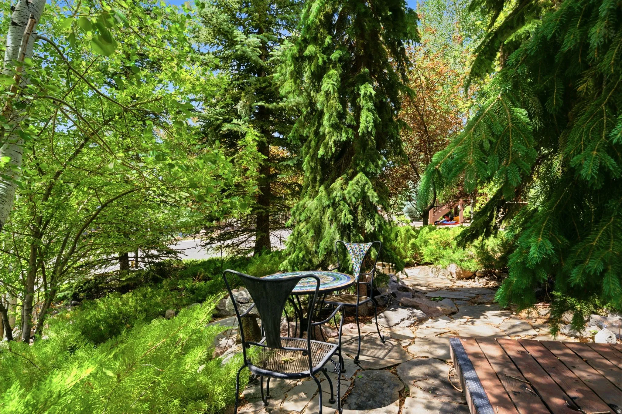 Outdoor living area featuring a flagstone patio, mature evergreen trees, and vibrant green foliage