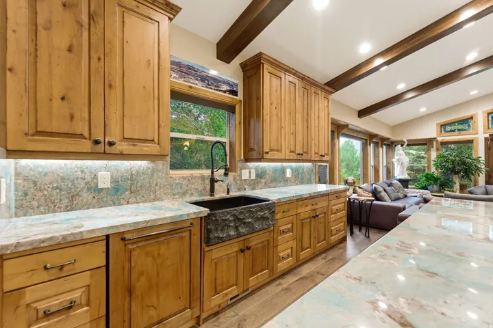 Kitchen featuring custom wood cabinetry, stone countertops, a large farm sink with a dark-finish faucet, and a coordinating stone backsplash