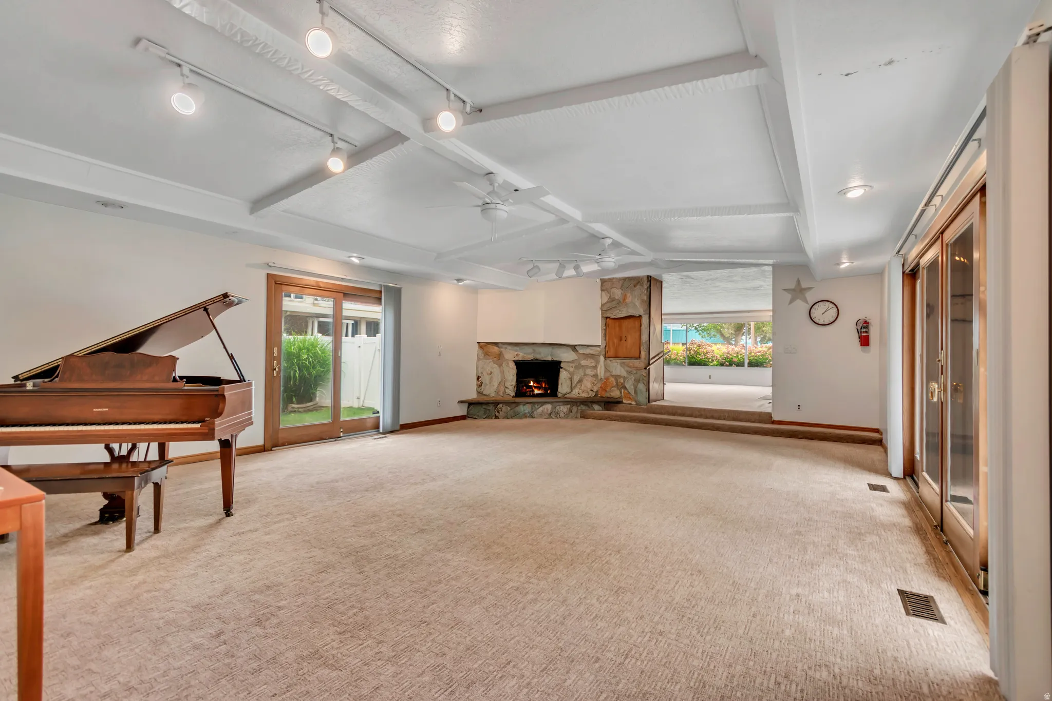 Spacious room featuring a stone fireplace, exposed beam ceiling with track lighting, and light-colored carpeting