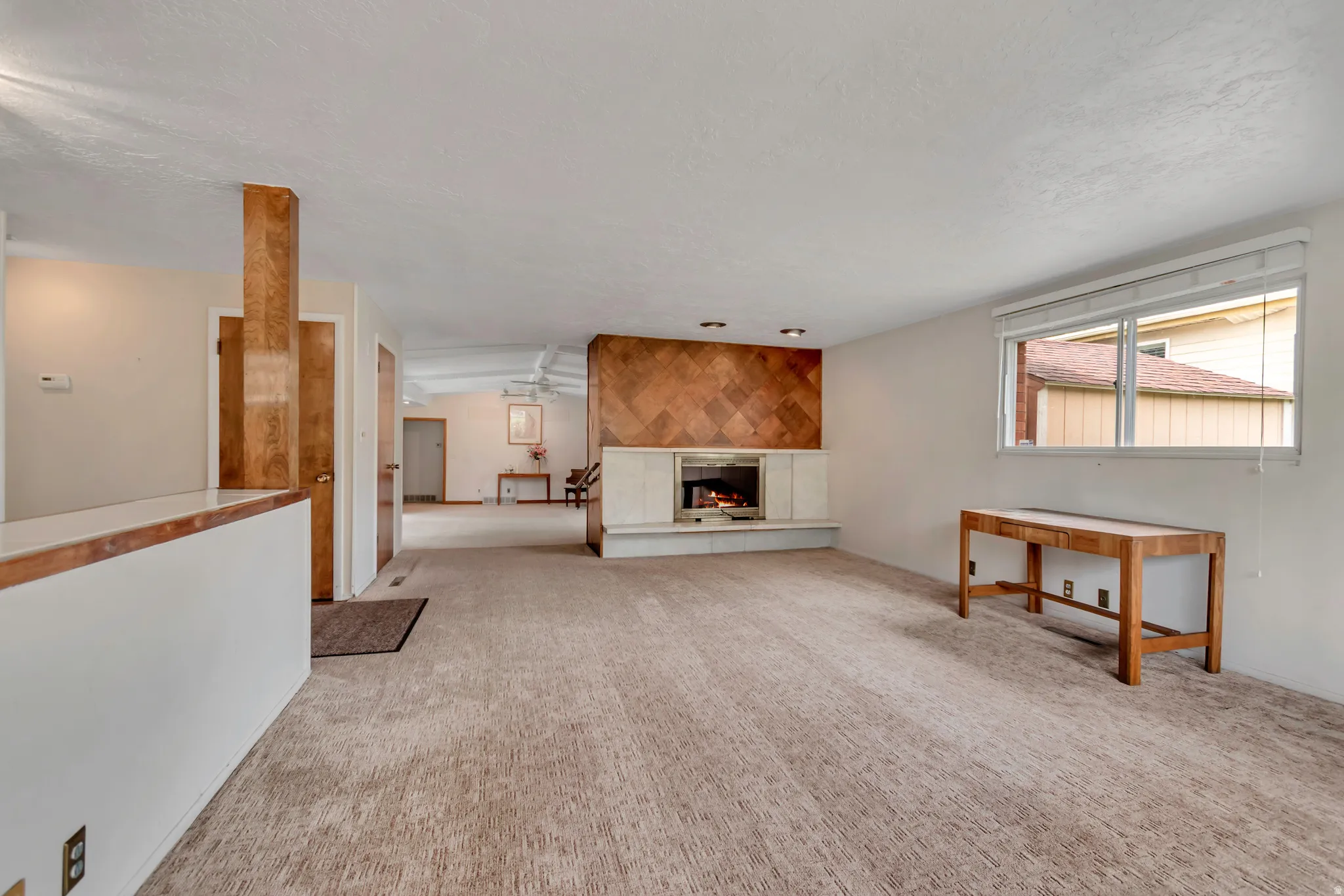 Living area featuring a fireplace with a tiled surround, and a large window with blinds