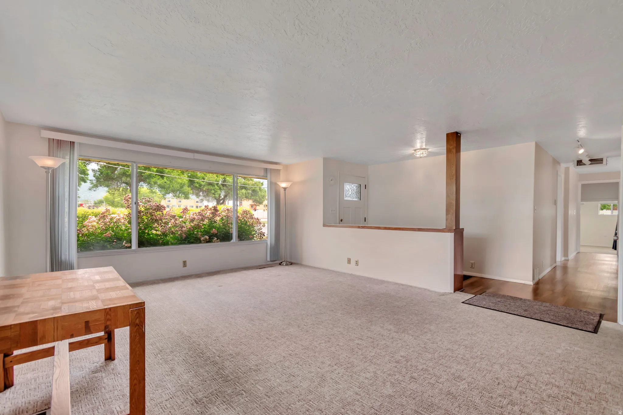 Expansive living area featuring a large picture window, carpet flooring, a half-wall partition with wood-finish trim, and showing the main entry door