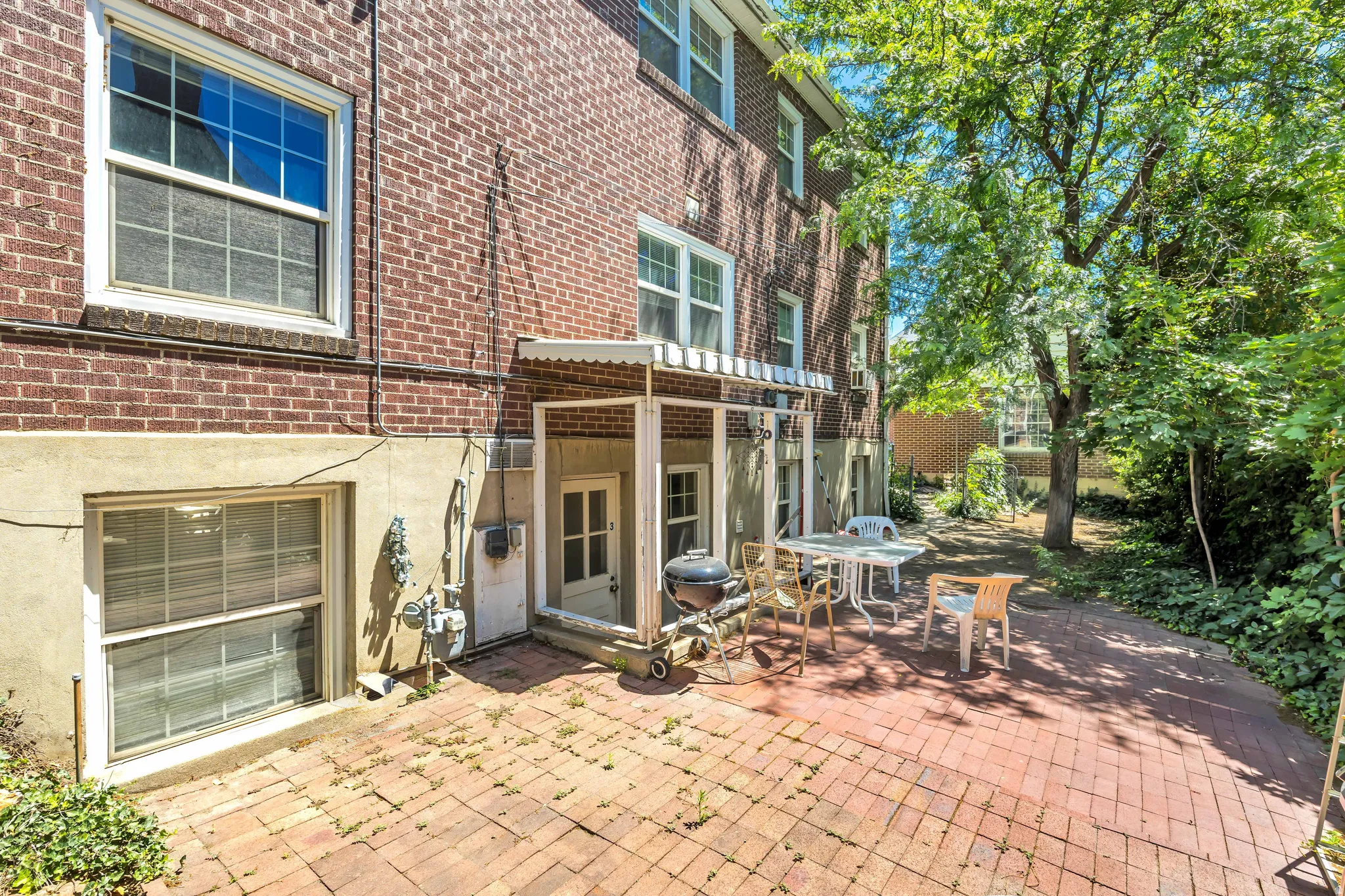 Brick exterior featuring a private brick patio area, mature trees, and landscaping