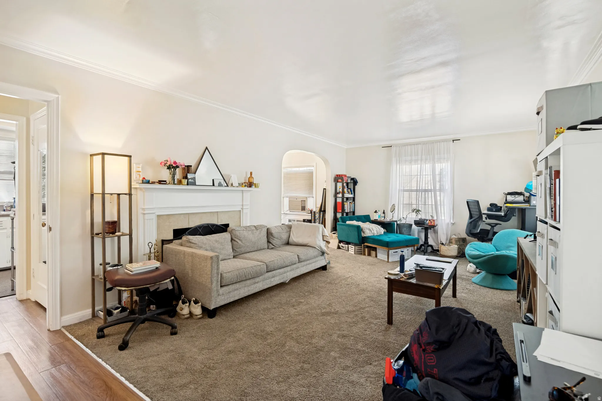 Unit 1 Spacious living room featuring a traditional fireplace with a white mantel, archway detailing, and crown molding