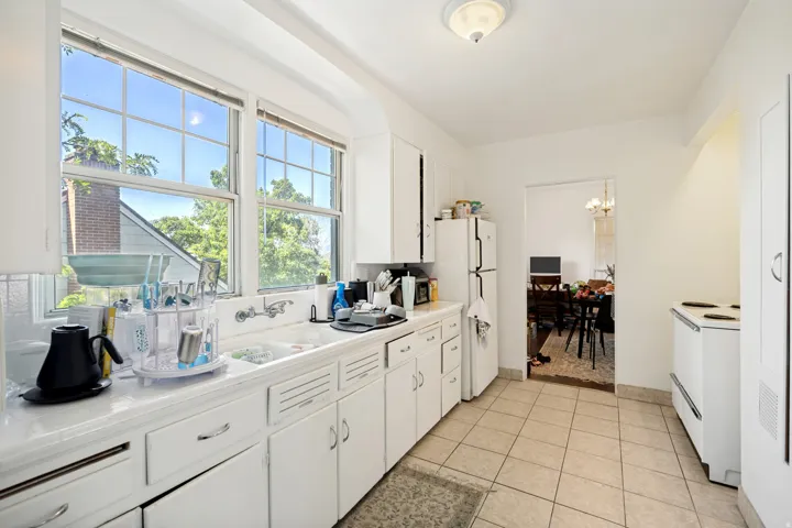 Unit 2  Bright kitchen featuring a large window, tile flooring, white cabinetry, integrated sink, and an arched doorway