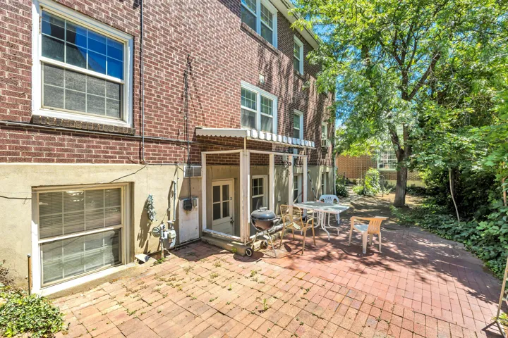 Brick exterior featuring a private brick patio area, mature trees, and landscaping
