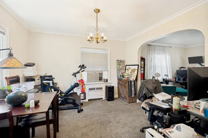 Unit 1 Carpeted interior space featuring a brass chandelier light fixture, crown molding, and an arched doorway