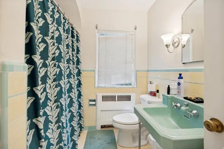 Unit 1 Bathroom featuring a light green basin sink, white toilet, and yellow and light blue tiled walls