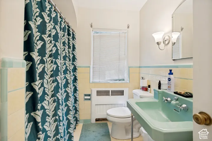 Unit 1 Bathroom featuring a light green basin sink, white toilet, and yellow and light blue tiled walls