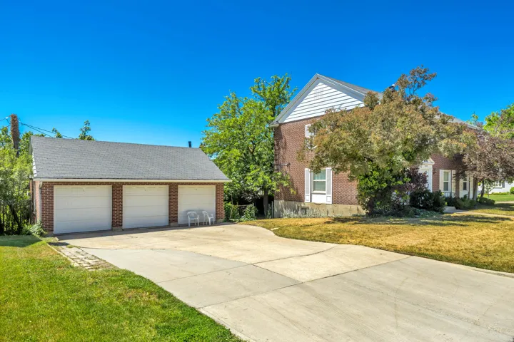 Expansive concrete driveway leading to a three-car detached garage with white paneled doors