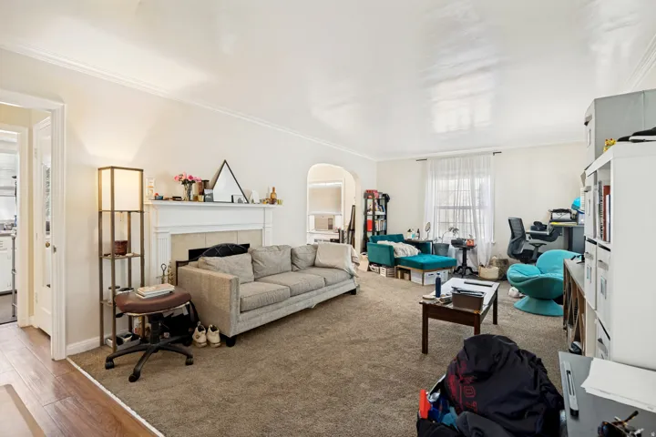 Unit 1 Spacious living room featuring a traditional fireplace with a white mantel, archway detailing, and crown molding