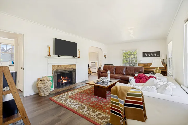 Unit 2 Living room featuring a fireplace with a stone surround and white mantelpiece, crown molding, dark wood-finish flooring, and a large window with natural light