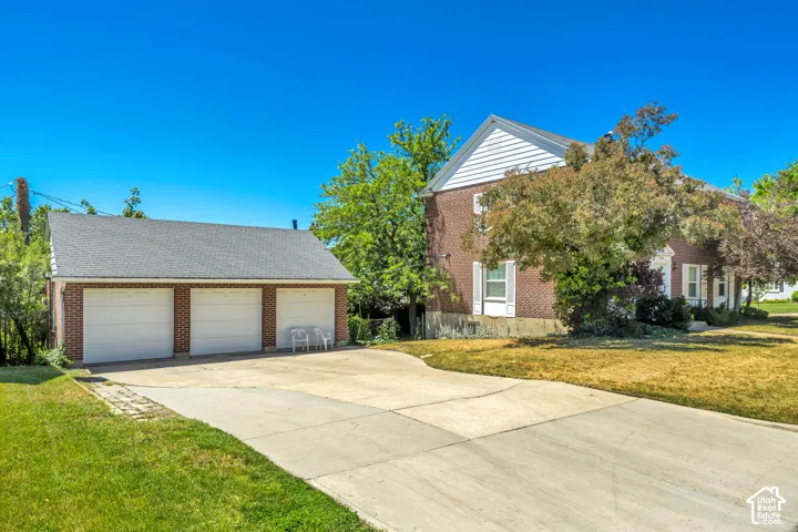 Expansive concrete driveway leading to a three-car detached garage with white paneled doors