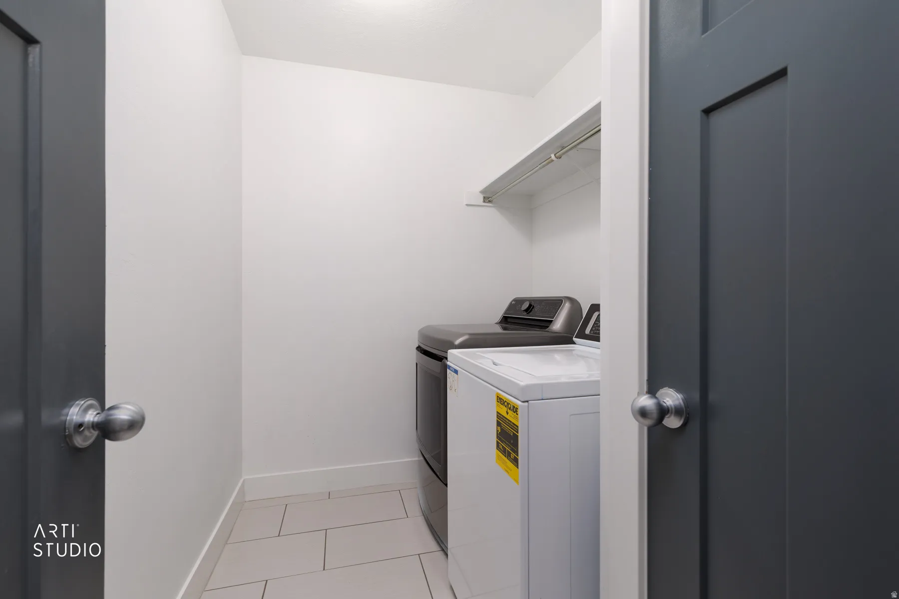 Dedicated laundry area featuring light-toned tile flooring, white walls, and a built-in wire shelf