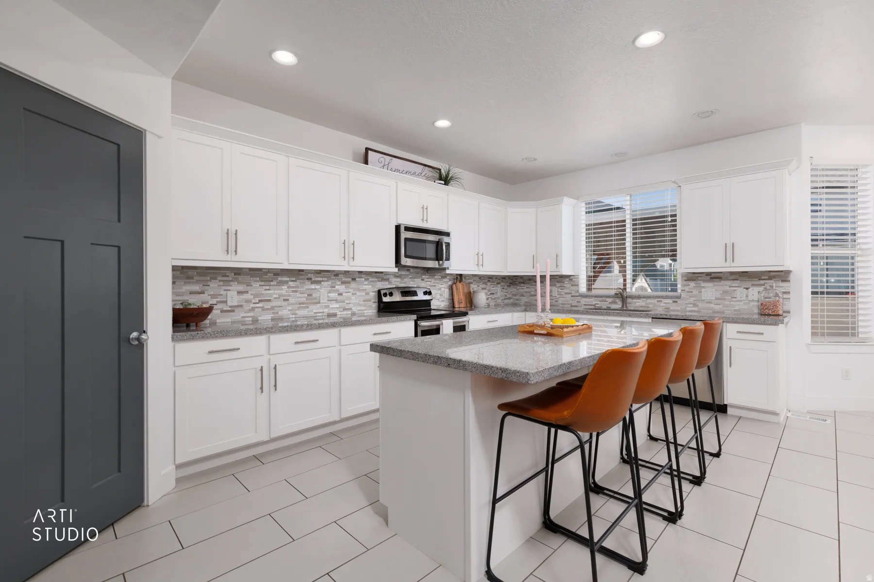 Bright kitchen featuring white cabinetry, a large center island with seating, stone countertops, and a tiled backsplash