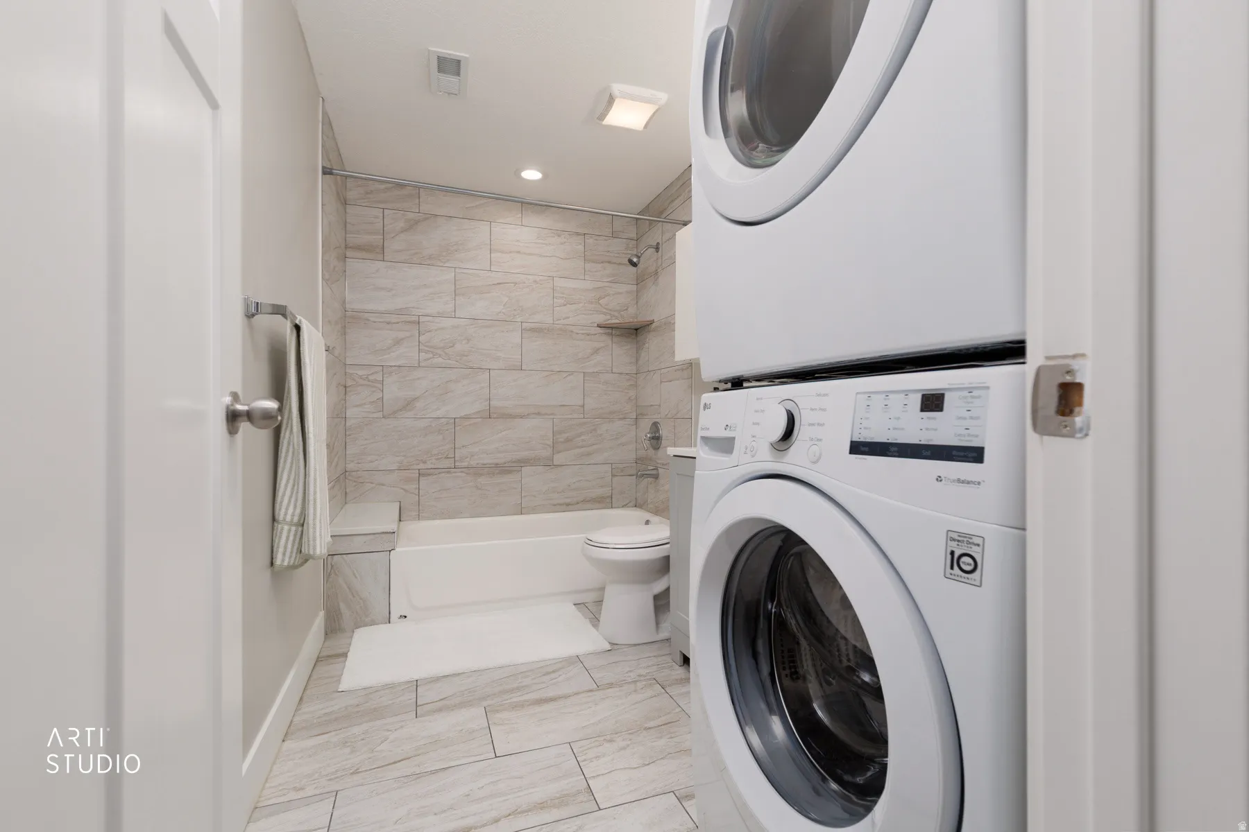 Bathroom featuring stacked washer and dryer unit, tiled flooring, and a bathtub with tiled surround
