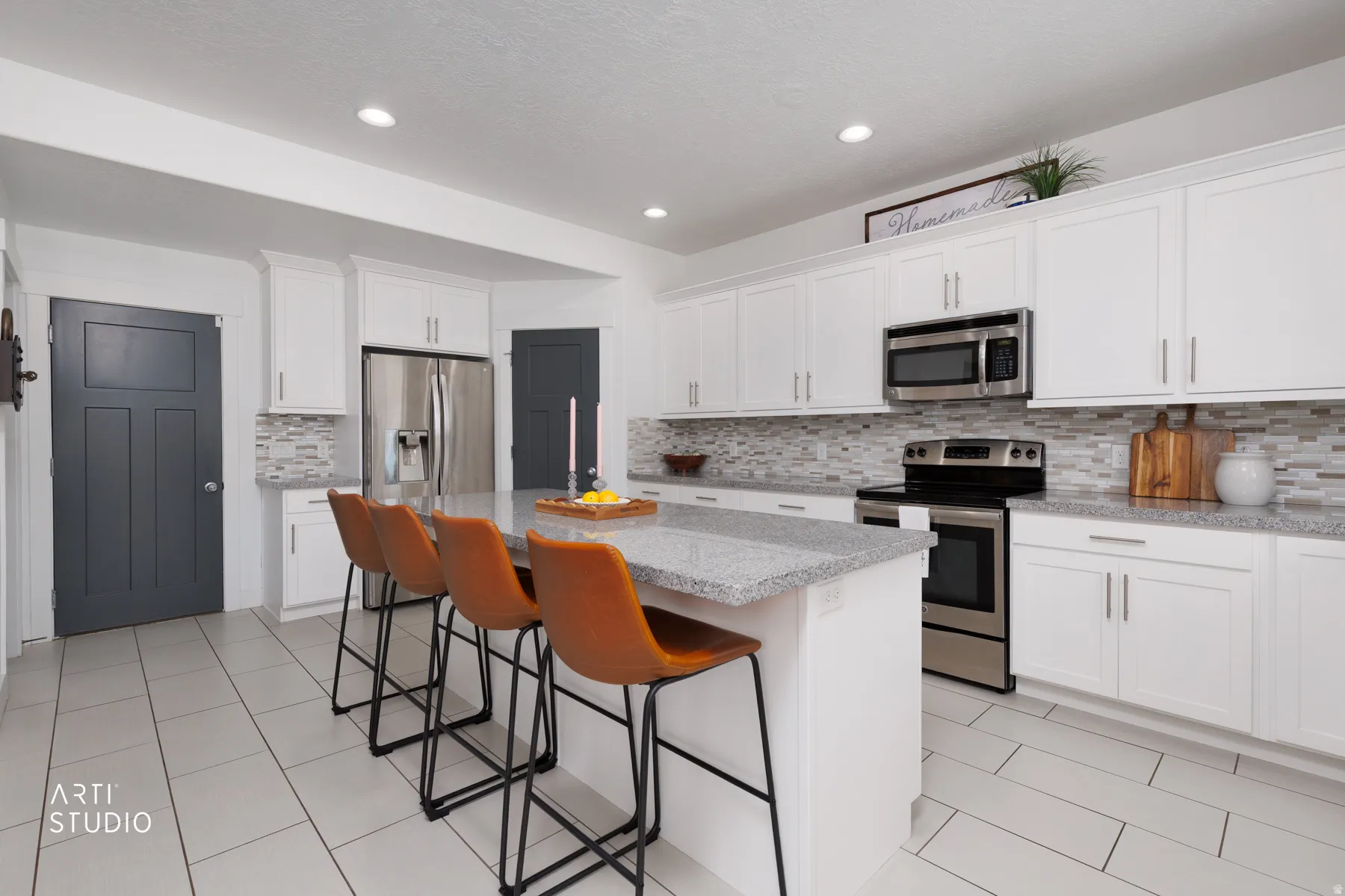 Kitchen featuring a central island with a light-colored countertop, white cabinetry, integrated stainless steel appliances, a tiled backsplash, and light-colored tile flooring
