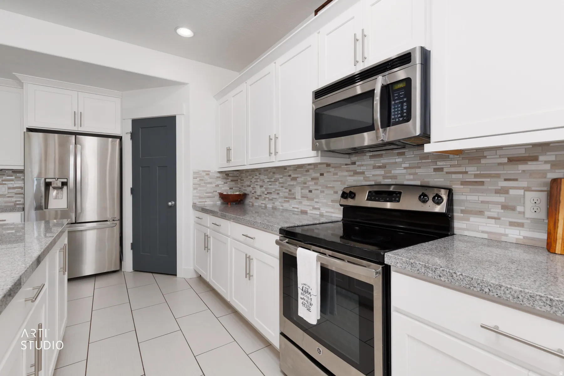 Kitchen featuring white shaker cabinetry, stainless steel appliances, speckled countertops, and a mosaic tile backsplash