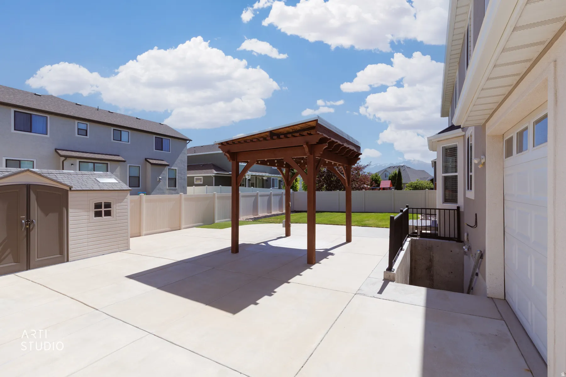Spacious concrete patio featuring a wooden pergola, leading to a landscaped lawn