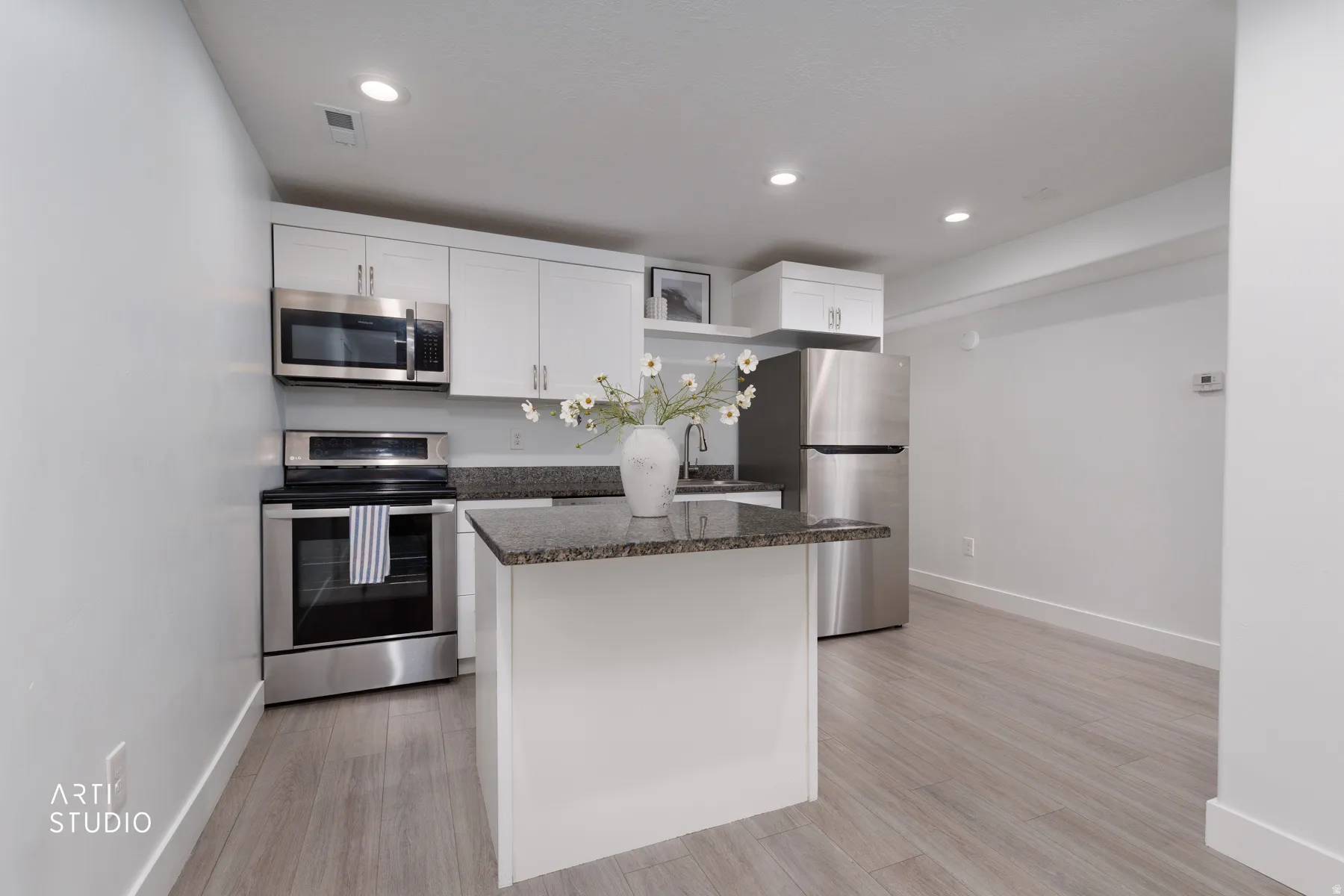 Full kitchen featuring stainless steel appliances, white cabinetry, granite countertops, a central island, and wood-finish flooring
