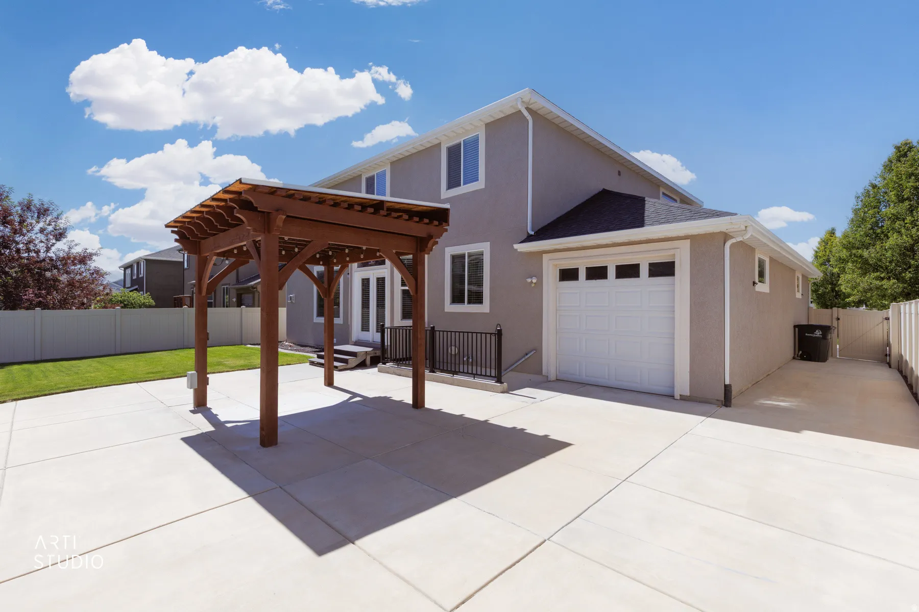 Spacious concrete patio featuring a wooden pergola, an expansive lawn area, and a white vinyl privacy fence