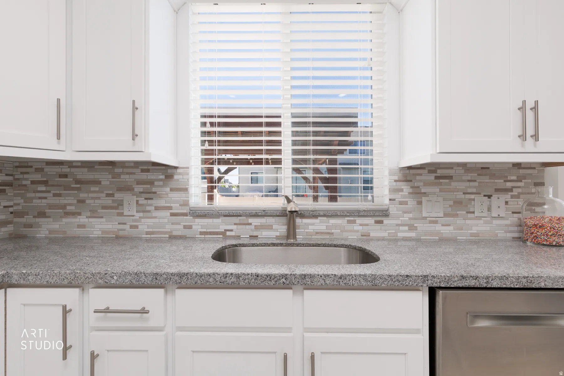 Kitchen featuring white shaker-style cabinetry, a stainless steel sink with a gooseneck faucet, light-toned countertop, and a mosaic tile backsplash