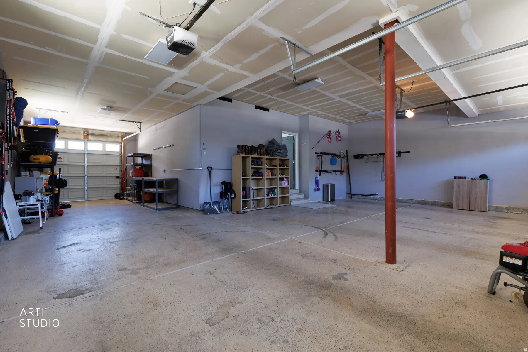 Spacious garage with concrete flooring, exposed ceiling joists, and multiple overhead lights