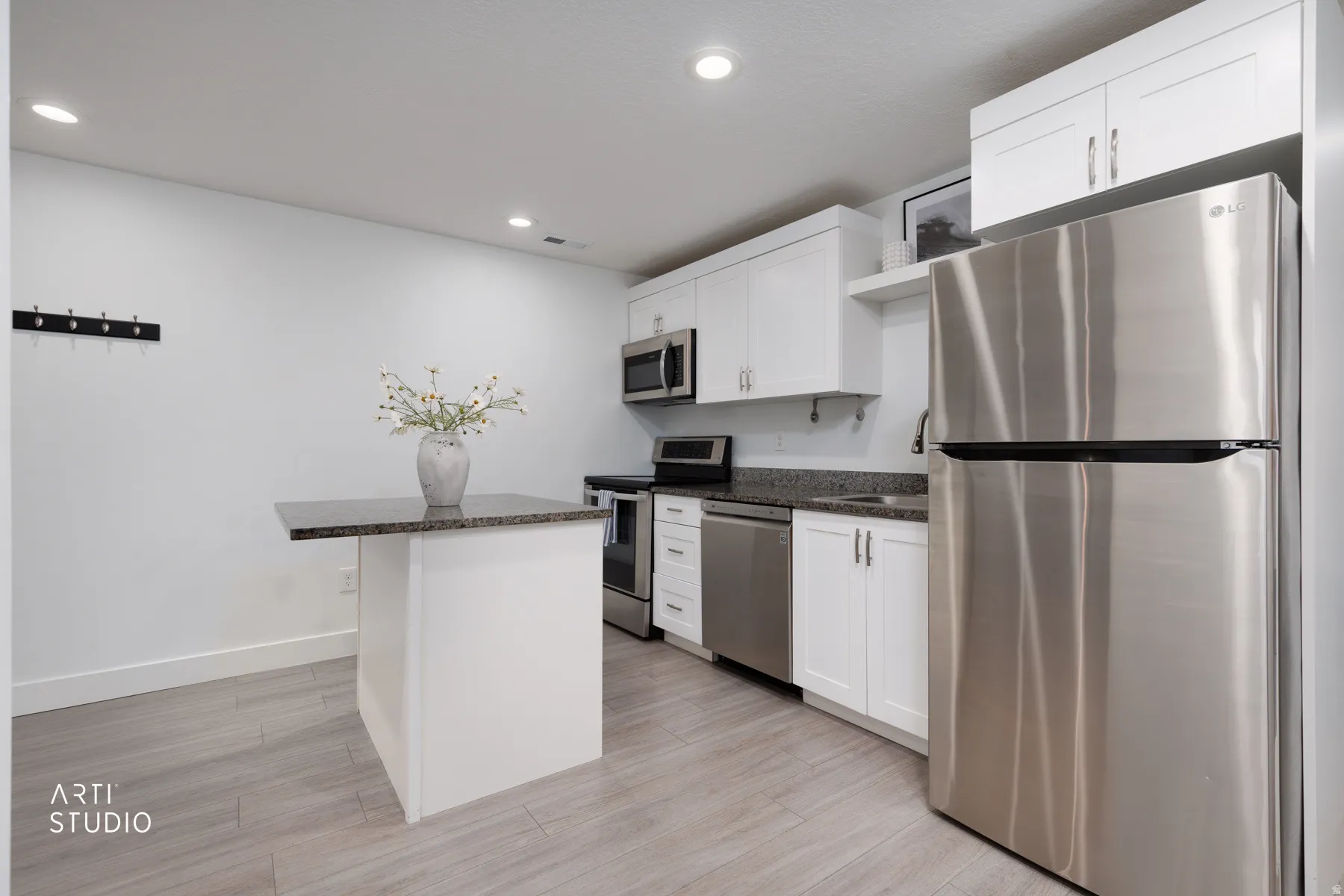 Contemporary kitchen featuring white cabinetry, stainless steel appliances, granite-style countertops, a freestanding island with an overhang, and wood-finish flooring