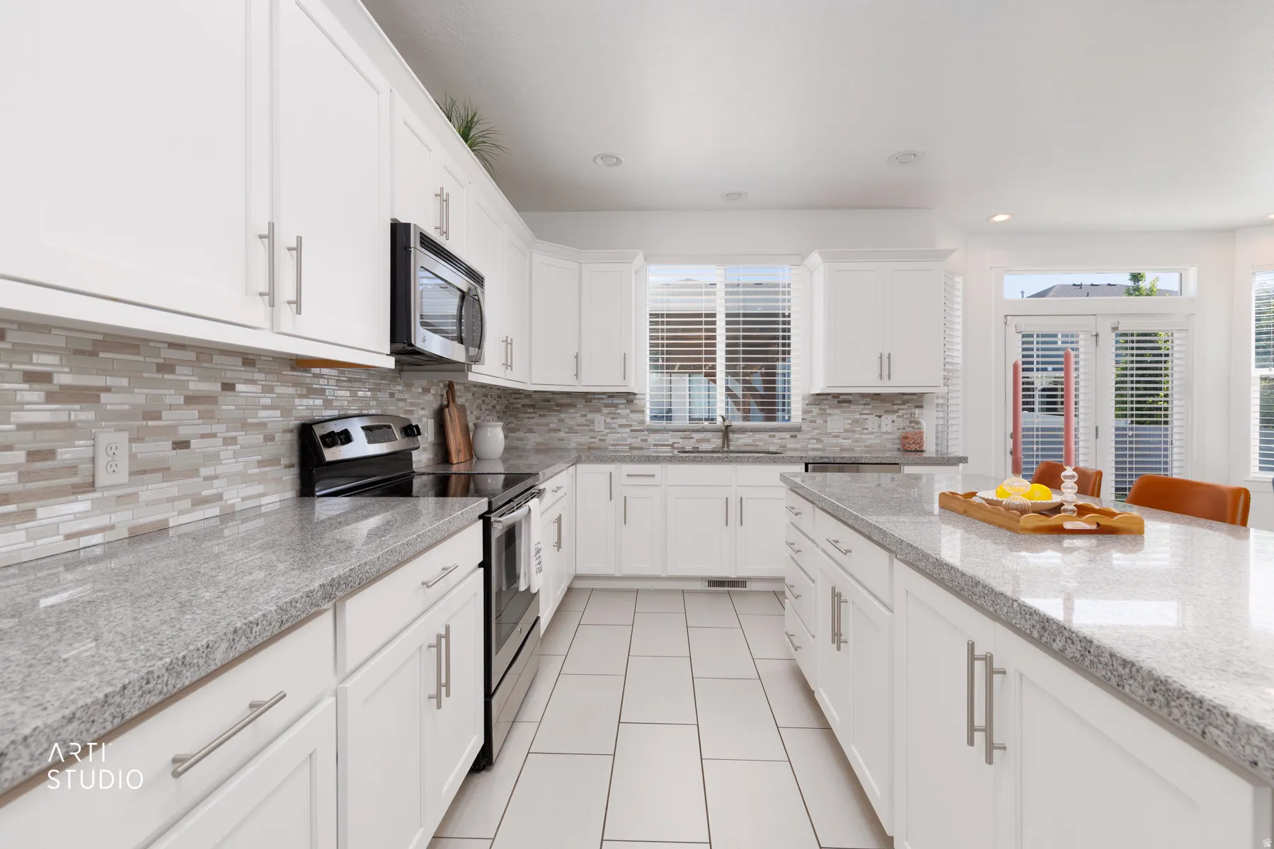 Contemporary kitchen featuring white cabinetry, light-toned countertops, a glass tile backsplash, stainless steel appliances, and a central island with bar seating