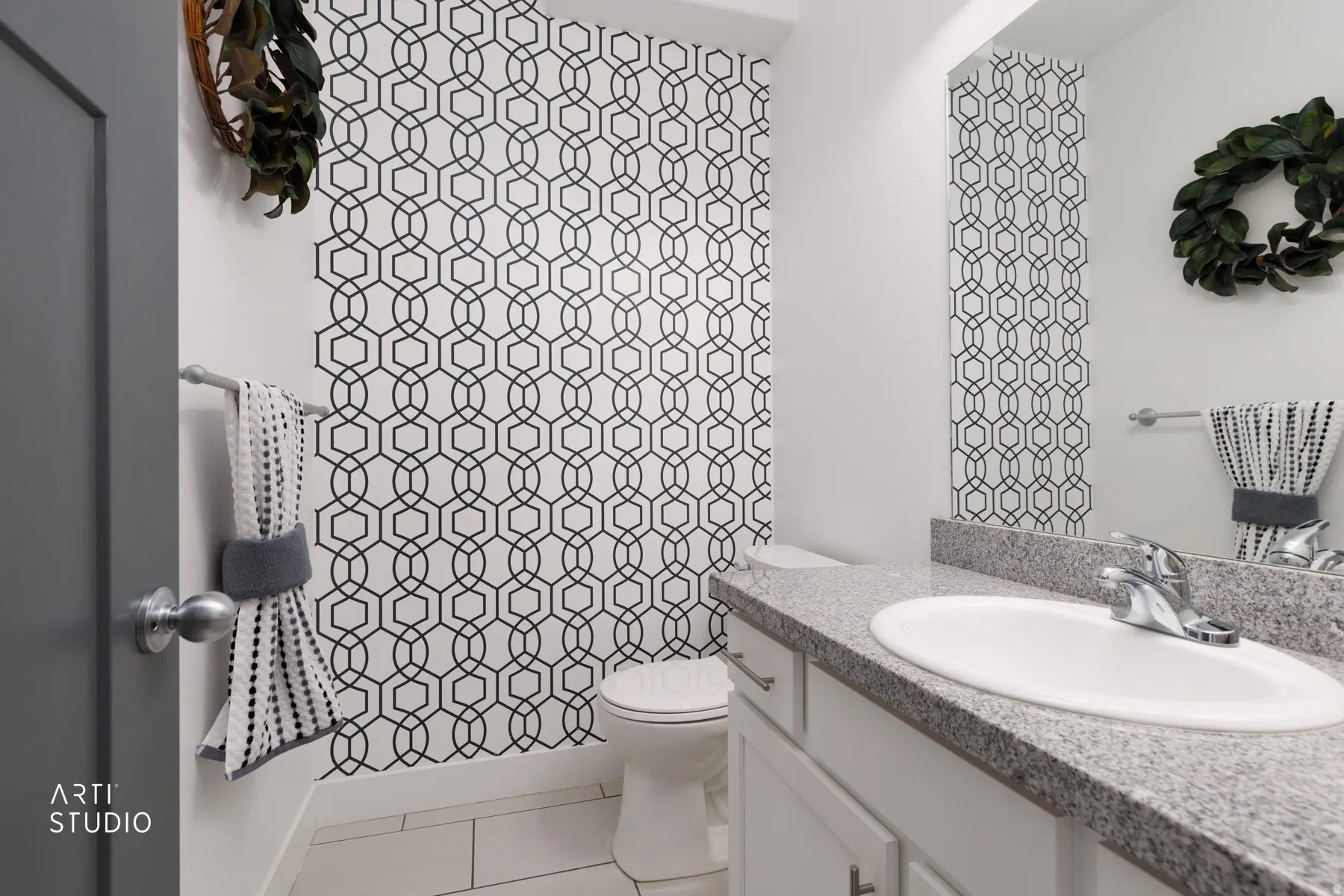 Powder room featuring a patterned accent wall, white vanity with a granite-finish countertop, and undermount sink with chrome fixtures