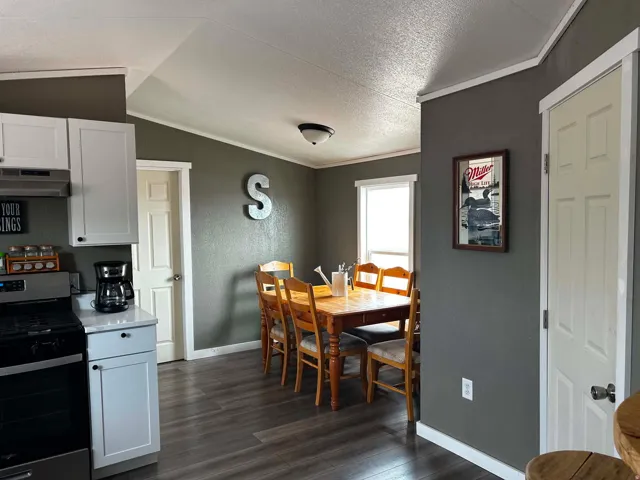 Kitchen and dining area featuring wood-finish flooring, white cabinetry with dark hardware, stainless steel range, and light-toned countertops