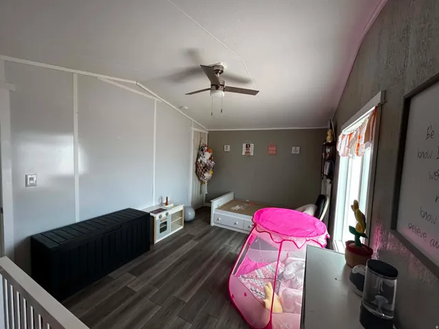 Room featuring wood-finish flooring, a sloped ceiling, and a ceiling fan