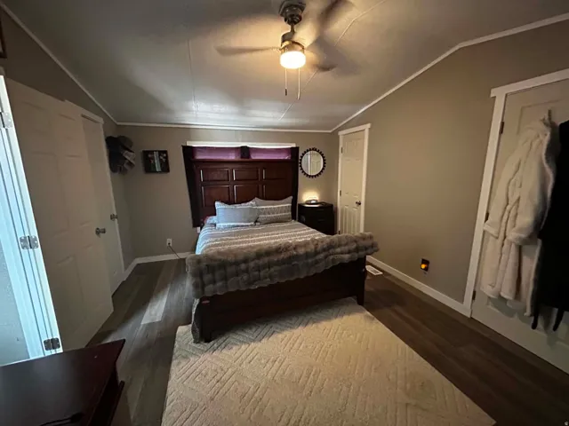Spacious master bedroom featuring wood-finish flooring, a ceiling fan with integrated lighting, and multiple panel doors with white trim