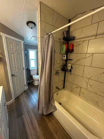 Master Bathroom featuring a white bathtub, large format tile surround with subtle veining, and wood-finish flooring