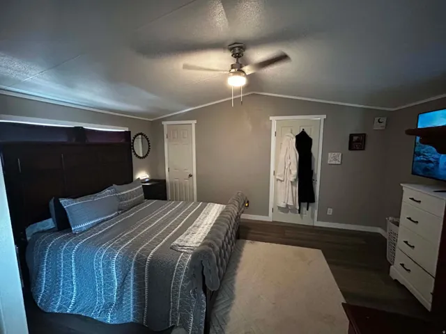 Master bedroom Vaulted ceiling bedroom featuring wood-finish flooring, a ceiling fan with integrated lighting, and crown molding