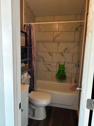 Bathroom featuring a white bathtub, ceramic tile surround with marble-look veining, a chrome showerhead, and wood-finish flooring