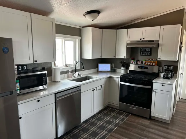 Kitchen featuring white shaker-style cabinetry, stainless steel appliances, a stainless steel sink with a matte black faucet, light-toned countertops, and wood-finish flooring