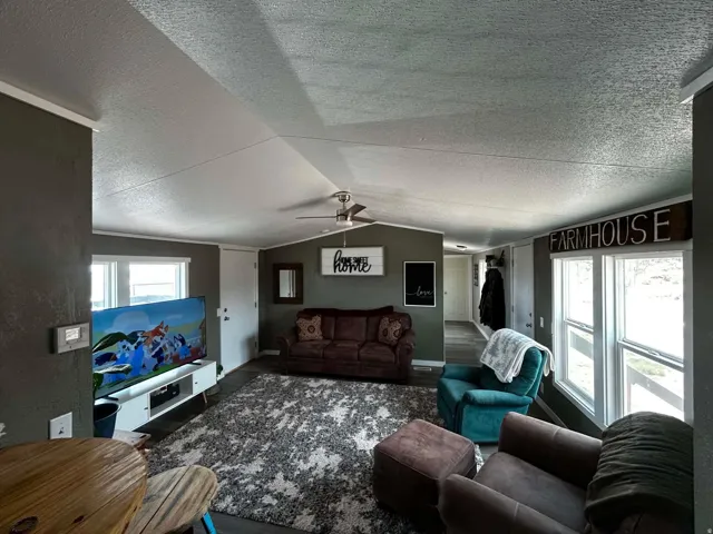 Spacious living area featuring wood-finish flooring, two large windows, a ceiling fan, and recessed lighting