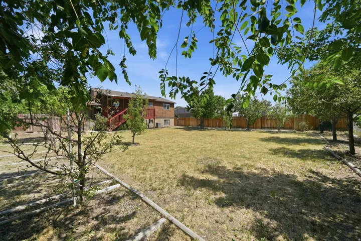 Spacious backyard with a wooden fence boundary, mature trees, and a multi-level deck with red stairs