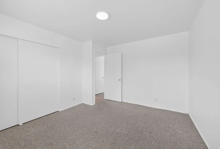 Neutral tone wall paint, flush mount ceiling light fixture, grey carpet flooring, white trim, and sliding closet doors