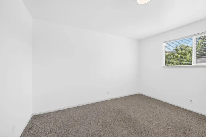 Neutral white walls with a ceiling-mounted light fixture, gray carpeting, and a window with horizontal blinds