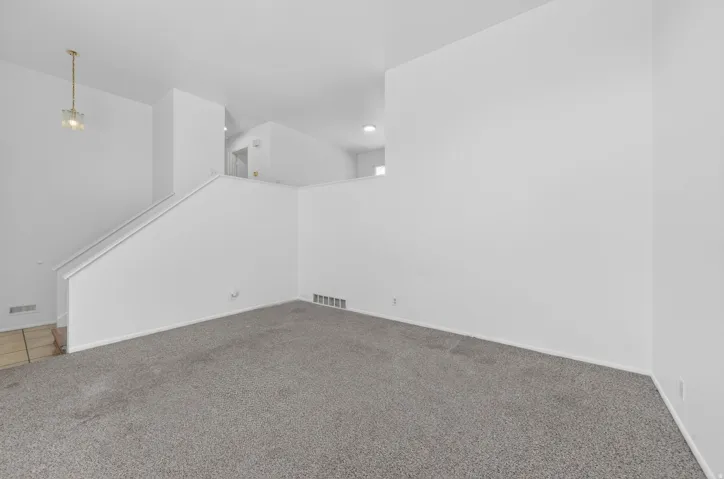 Spacious interior featuring a neutral color palette, grey carpeting, white baseboards, and a contemporary chandelier