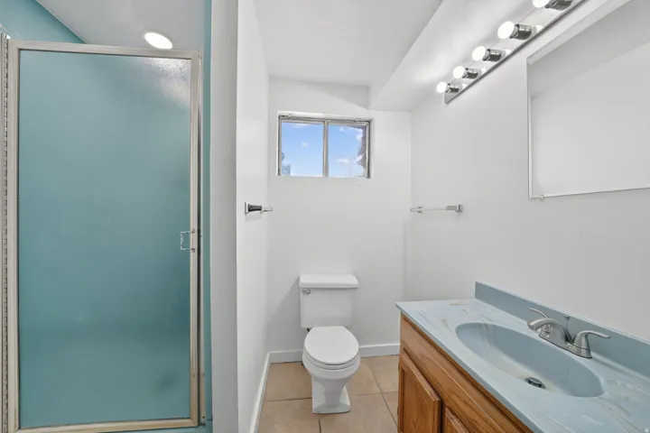 Bathroom featuring a shower with a translucent glass enclosure, a vanity with a light blue countertop and integrated sink, a chrome faucet, a white toilet, and a window