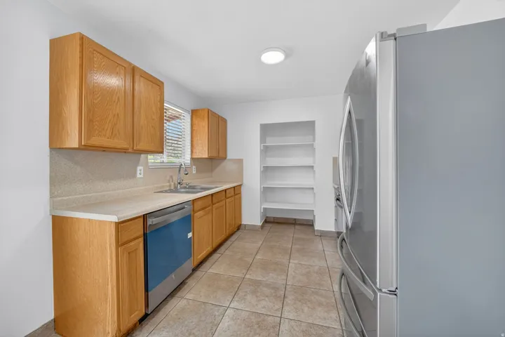 Functional kitchen featuring light wood-finish cabinetry, a stainless steel dishwasher, and a double basin sink