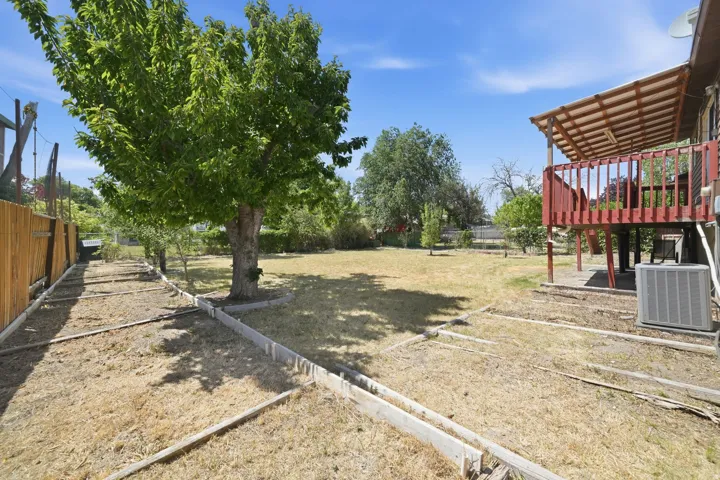 Expansive backyard featuring a mature central tree, a wooden privacy fence, raised garden beds, and an elevated deck with a slatted roof