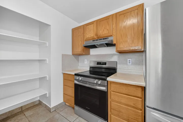 Kitchen featuring a stainless steel range, light wood cabinetry, light-toned countertops, and a full-height pantry with white shelving